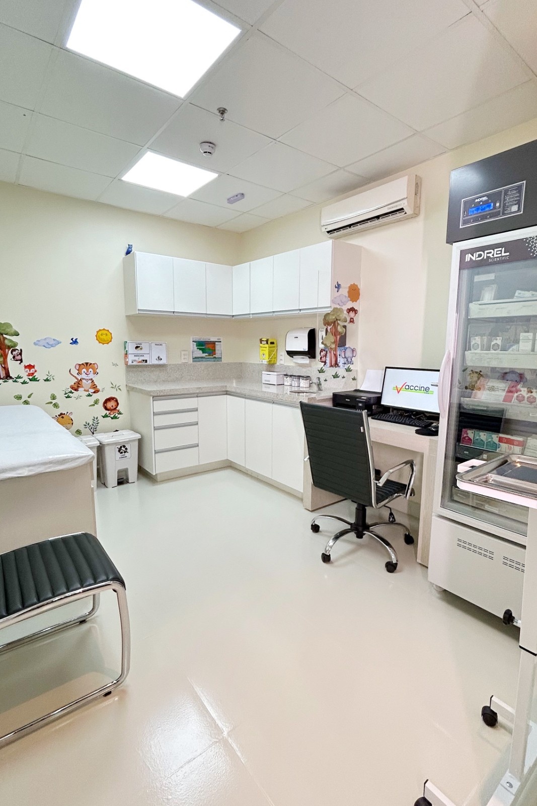 Sala de aplicação da Vaccine Care Arujá, com maca, bancada e geladeira de vacinas